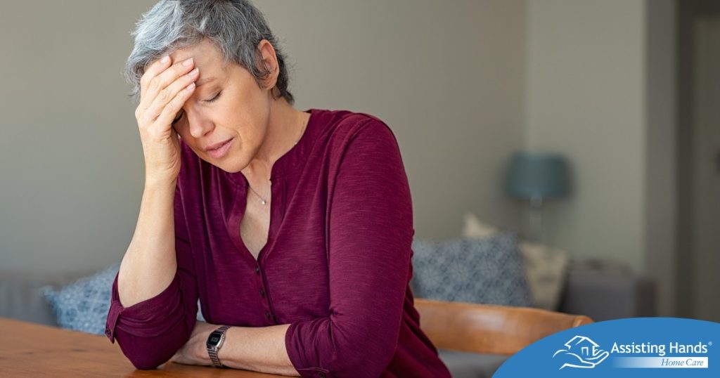 A woman holds her head in her hand, representing the stress that new family caregivers go through.