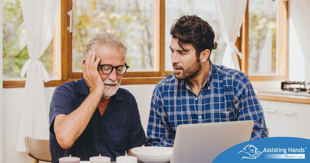 A man looks at a computer with his father who is confused, representing one of the early signs of dementia.