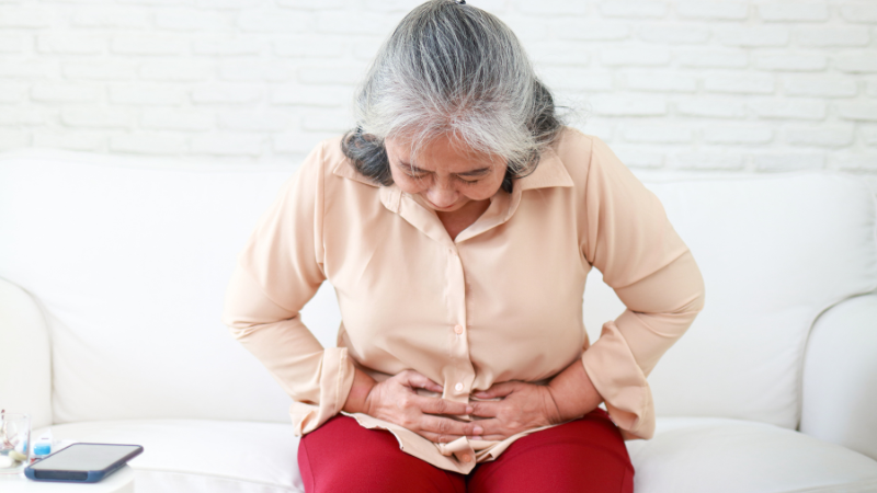 elderly woman Sitting on Sofa and Touching Belly Writhing in Pain