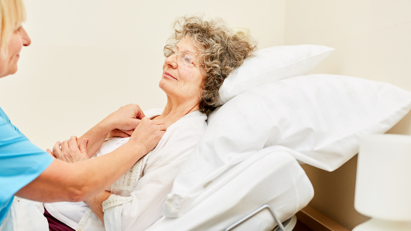caregiver is taking off an elderly woman shirt to help them bathe them on bed