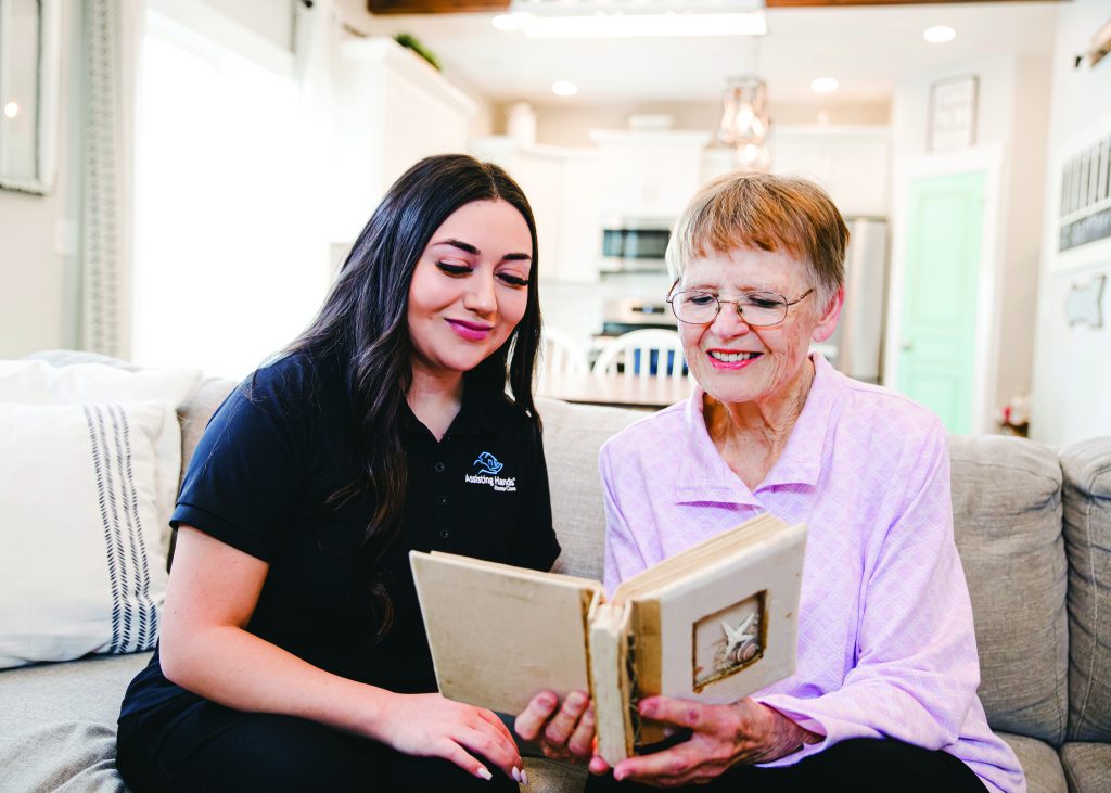 Assisting Hands caregiver and an elderly woman reading a book together