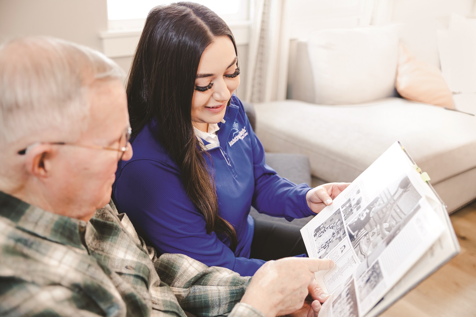 Assisting Hands caregiver and an elderly man looking at album together Assisting Hands caregiver and an elderly man looking at album together