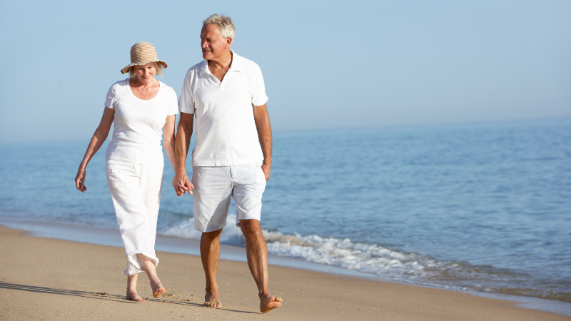 Senior snowbird couple walking along a beach in Florida - Assisting Hands