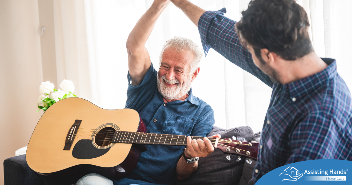A smiling son high fives his happy elderly father as he plays the guitar, showing the positive effect music can have on people, including those with dementia.