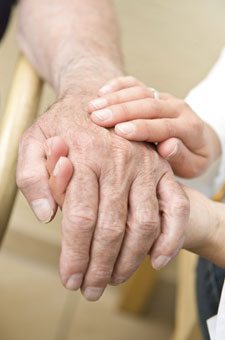 Caregiver gently holding a senior’s hands, providing support and reassurance for fall prevention.