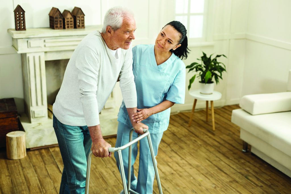 Senior man using a walker safely at home with a caregiver nearby, demonstrating fall prevention tips in Davis County home care