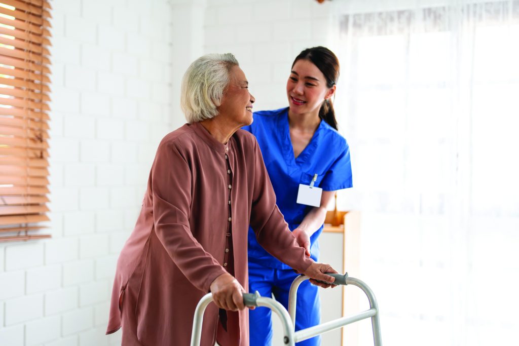Caregiver helping senior woman walk safely down hallway with walker in a bright, tidy home.
