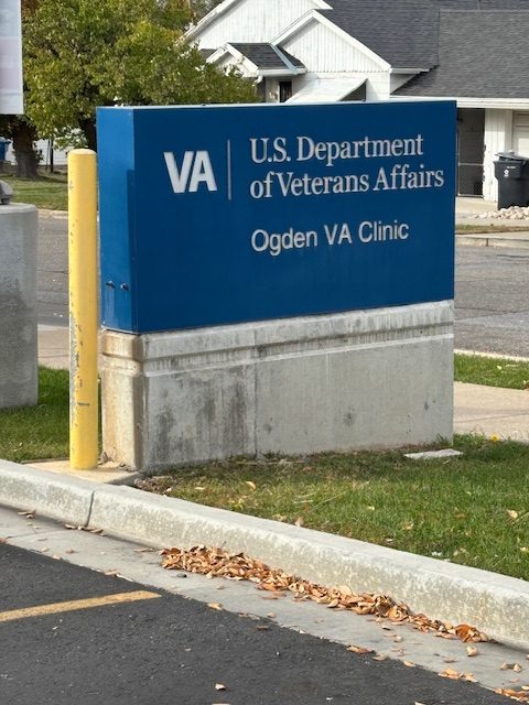 Blue U.S. Department of Veterans Affairs sign reading “Ogden VA Clinic” near the facility entrance in Ogden,