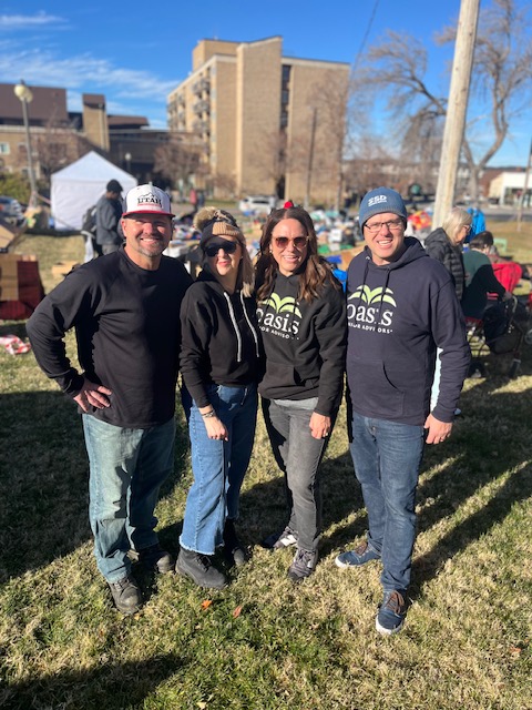 Assisting Hands Home Care and Oasis Senior Care team members pose together at Christmas in the Park in Ogden, Utah on a sunny winter day.