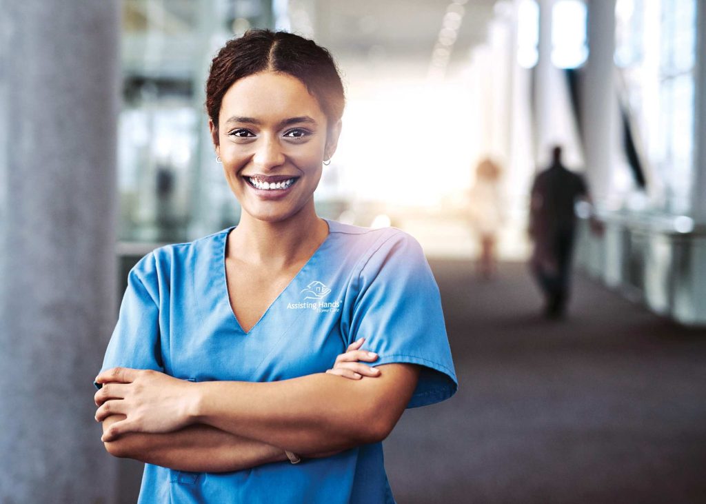 Professional home care caregiver smiling while wearing scrubs, representing compassionate in-home senior care in Davis County, Utah.