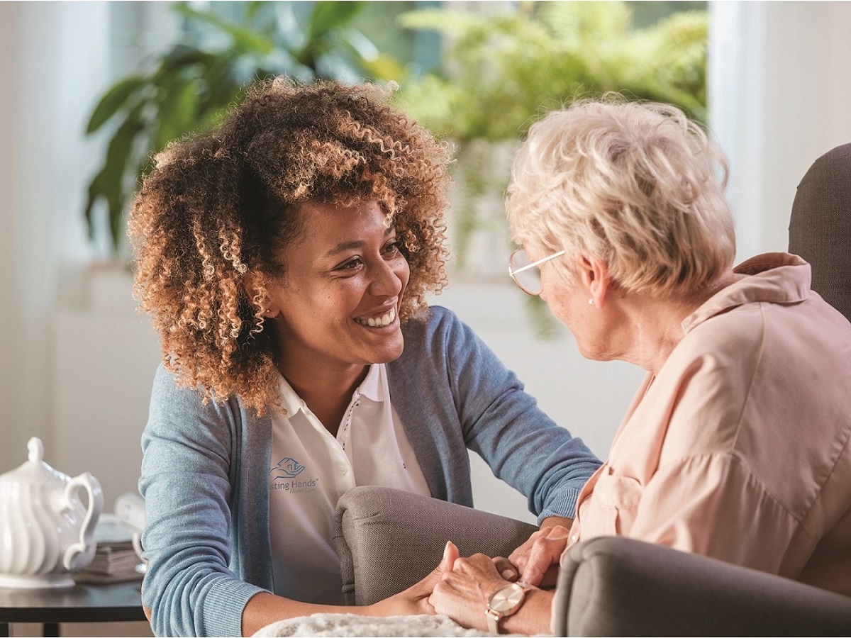 Caregiver sitting with an older woman in her Bulverde living room, holding her hands as they talk