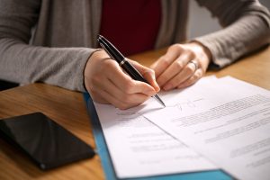 A close-up of a person's hands signing an important document at a wooden desk. Activating your long-term care insurance for home care is an important decision that should not be delayed. Families seeking in-home care in Murray, UT can use their existing LTCi policy to help cover the cost of quality care.
