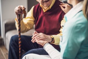 A caregiver sits beside an elderly man with a cane, gently holding his hands in a warm and supportive interaction. This kind of compassionate support is exactly what long term care insurance home care is designed to fund when the time is right. For those with long-term care insurance in Murray, UT, understanding your ADL triggers is the first step toward accessing the senior home care in Murray, UT that your policy was built to provide. 