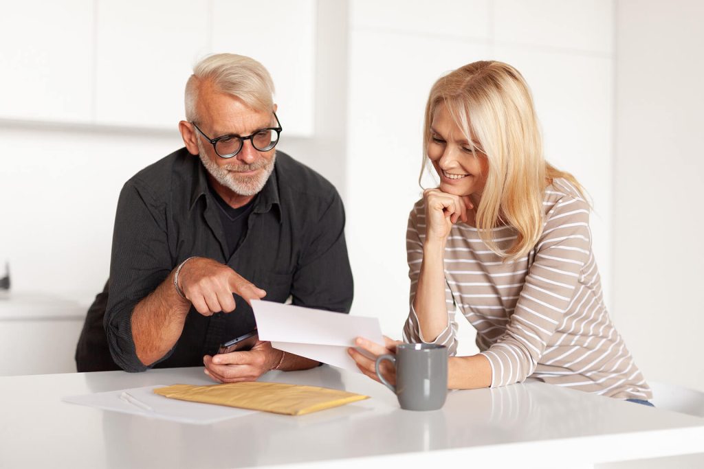 A middle-aged couple sits together at a table, smiling as they review documents, representing the process of understanding long-term care insurance in Murray, UT. Taking the time to carefully review your policy is one of the most important steps in making the most of your long term care insurance home care benefits. Families navigating LTCI in Murray, UT can benefit greatly from understanding their coverage before a care need becomes urgent.