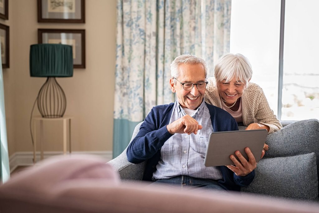 A senior couple laughs together while exploring a tablet from the comfort of their home, reflecting the joy and independence that aging in place in Murray, UT can provide with the right technology and support. Smart devices are just one of many tools that an aging in place specialist in Murray, UT can help families incorporate into a safe, sustainable home care plan. With the right setup, seniors can stay connected, engaged, and comfortable right where they belong.