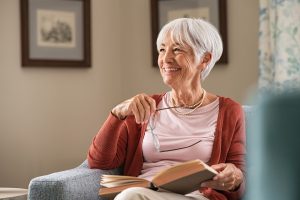 A senior woman smiles warmly while relaxing at home with a book, embodying the comfort, independence, and quality of life that aging in place in Murray, UT is all about. With the right combination of technology, home modifications, and in home care for seniors in Murray, UT, this kind of peaceful, independent lifestyle is well within reach. Assisting Hands is here to help make that vision a reality for your family. 