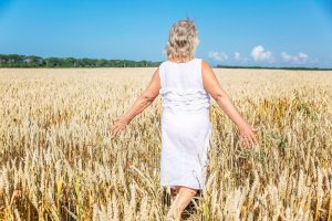 An older woman in a white dress walks freely through a golden wheat field with her arms outstretched, evoking the independence and quality of life that compassionate dementia care near me Murray, UT is designed to protect. Staying active and engaged outdoors is one of the many ways families and caregivers support brain health alongside professional Alzheimer's care in Murray, UT. 
