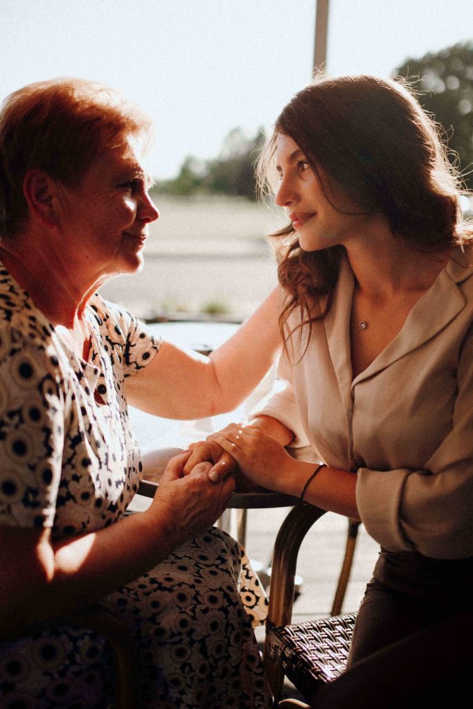 A mother and daughter sit close, holding hands and smiling warmly in the sunlight, a picture of the connection that respite care Murray helps protect. By easing caregiver burnout in Murray, UT and offering a senior caregiver in Murray, UT to share the load, families get to enjoy moments like this again.
