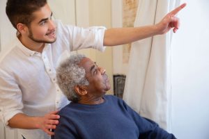 A young caregiver smiles and points toward the window while a senior man looks on with interest, the two sharing an ordinary, joyful moment of connection and companionship. Good care is about more than tasks, and it shows in exchanges like this one. Caregiver services in Murray, UT from at home caregivers pair dependable 24/7 home care with the genuine companionship that helps seniors feel truly at home. 
