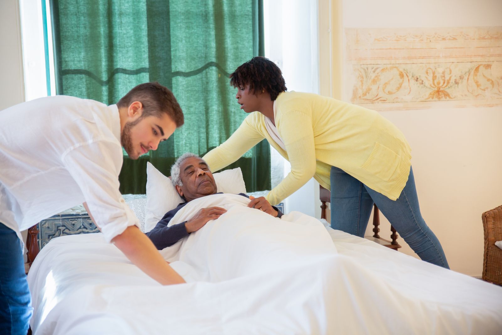 Two caregivers helping an older man rest comfortably in bed