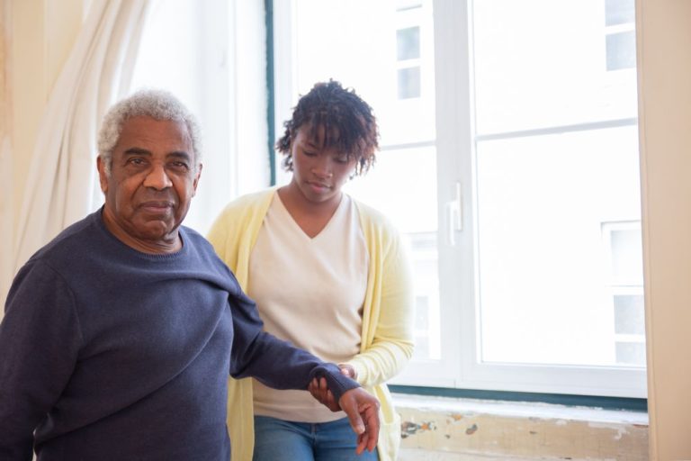 Caregiver keeping an older man company by a sunny window