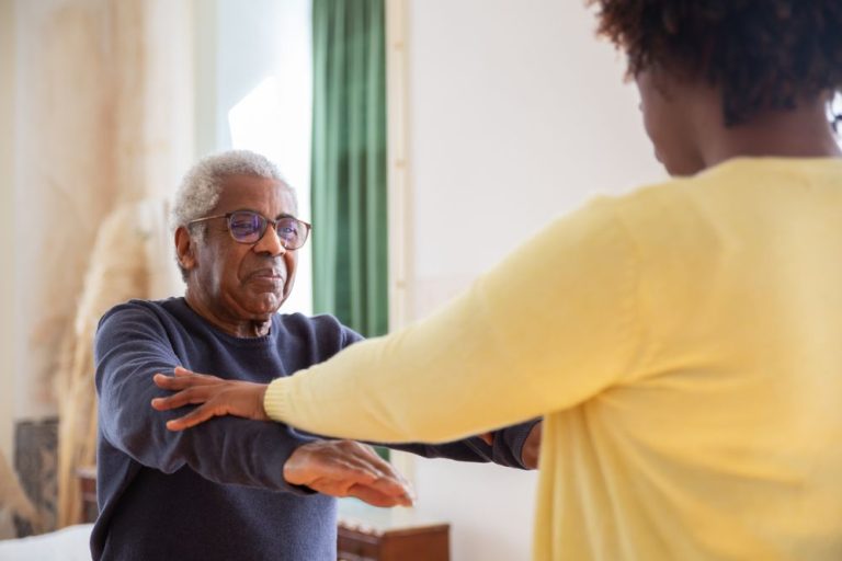 Caregiver helping an older man with gentle exercises at home