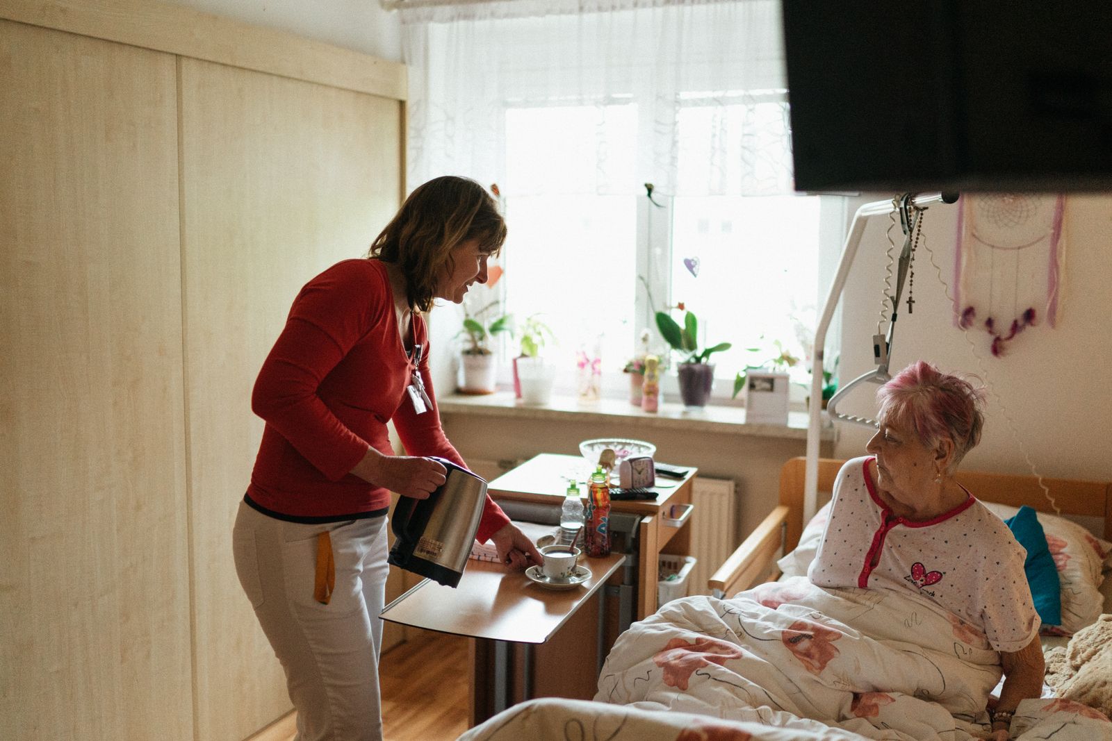 Caregiver bringing tea to an older woman at home during an hourly visit