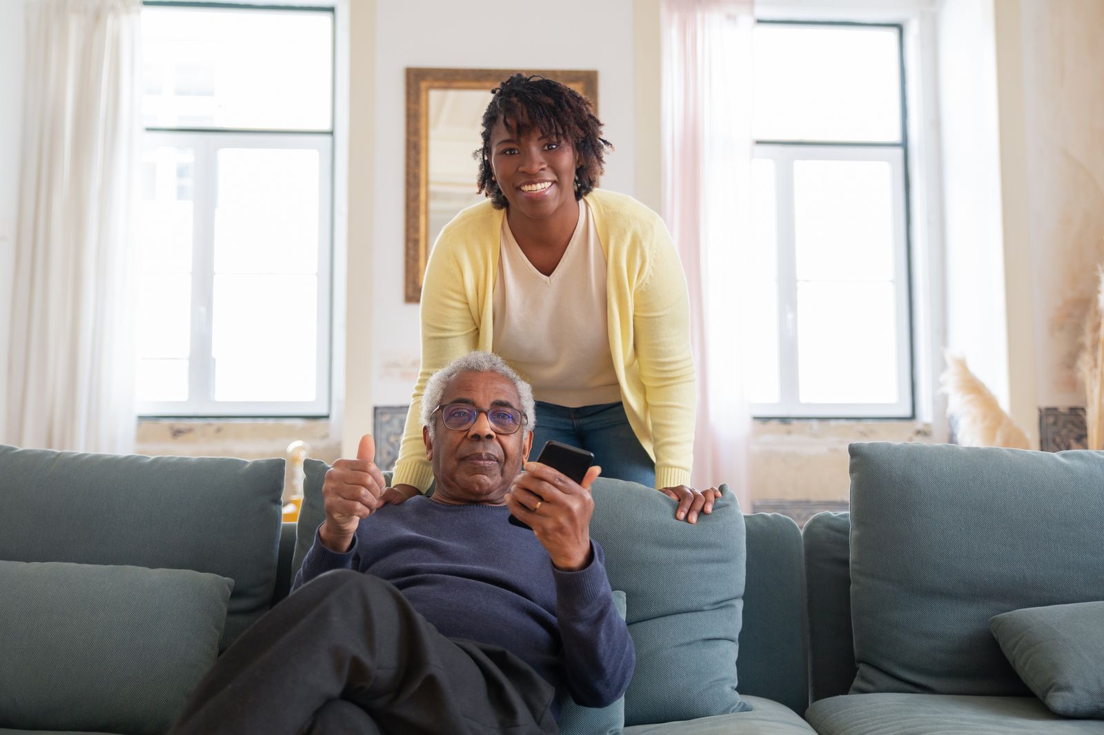 Caregiver with a smiling older man relaxing on his sofa