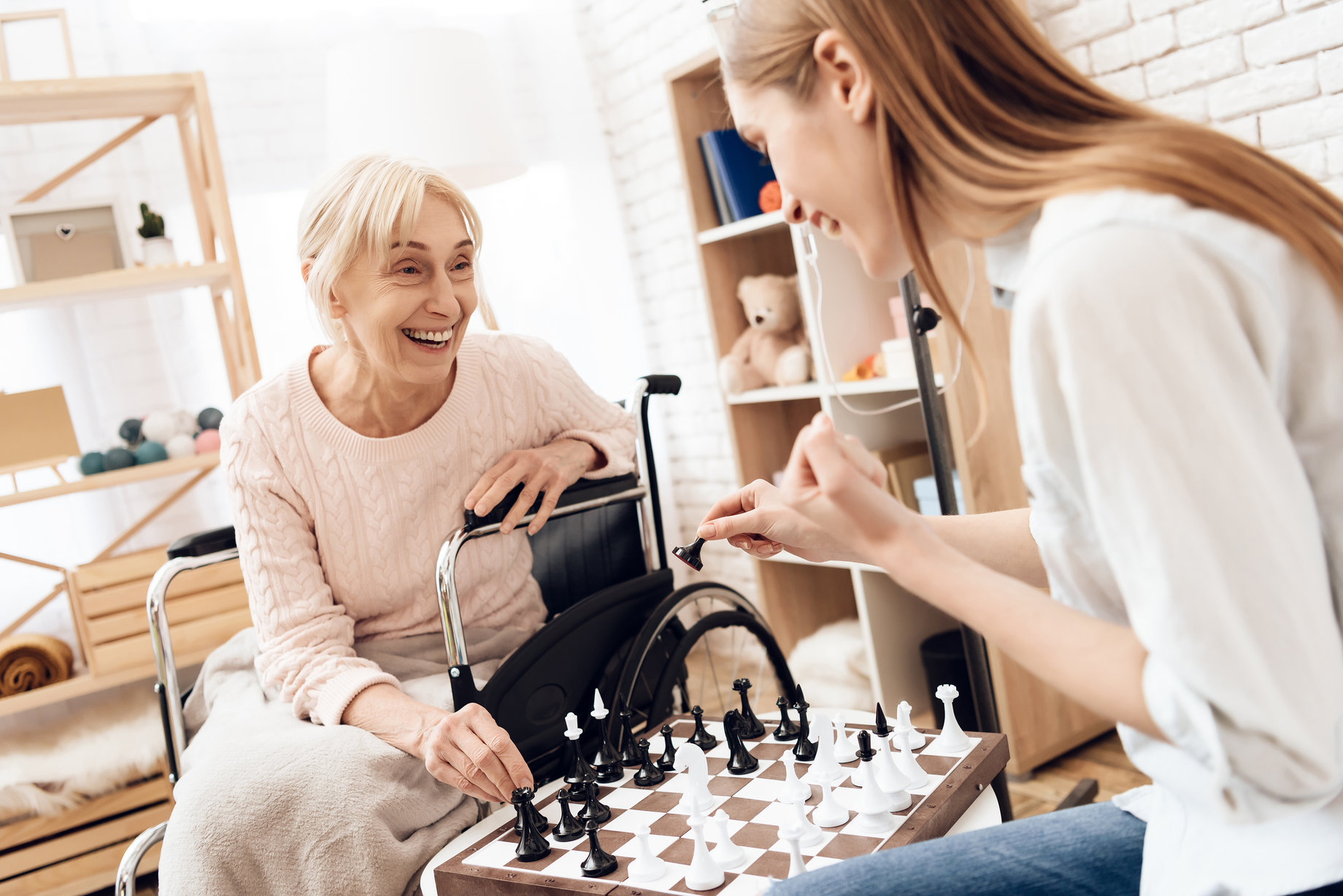 Girl is nursing elderly woman at home. They are playing chess.