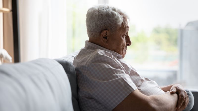senior man feeling lonely and depressed and sitting alone by himself on the couch