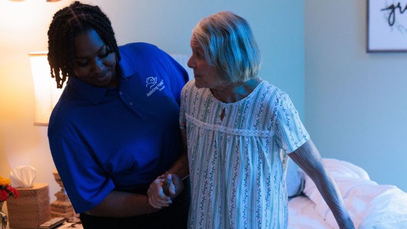 Assisting Hands live in caregiver helping senior woman walk to the bathroom at night
