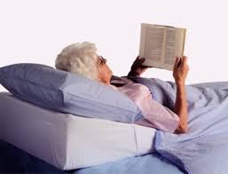 Elderly woman in bed propped up reading a book