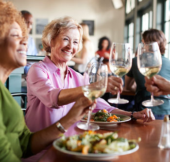 Two Smiling Senior Women Making A Toast At Meal In Restaurant
