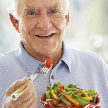 Senior Man Smiling At Camera And Eating Salad