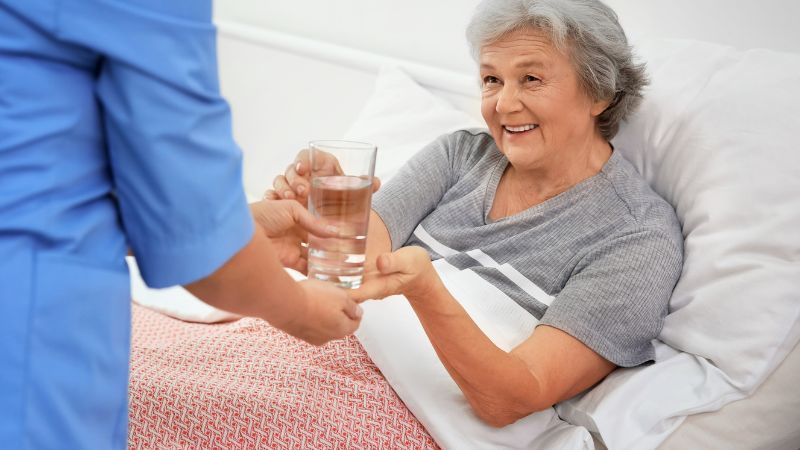 Assisting Hands Caregiver Giving a Glass of Water to Senior Woman