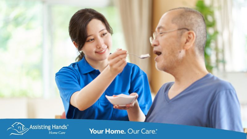 Assisting Hands Caregiver Feeding Senior Man at Home Post Stroke Hospitilization