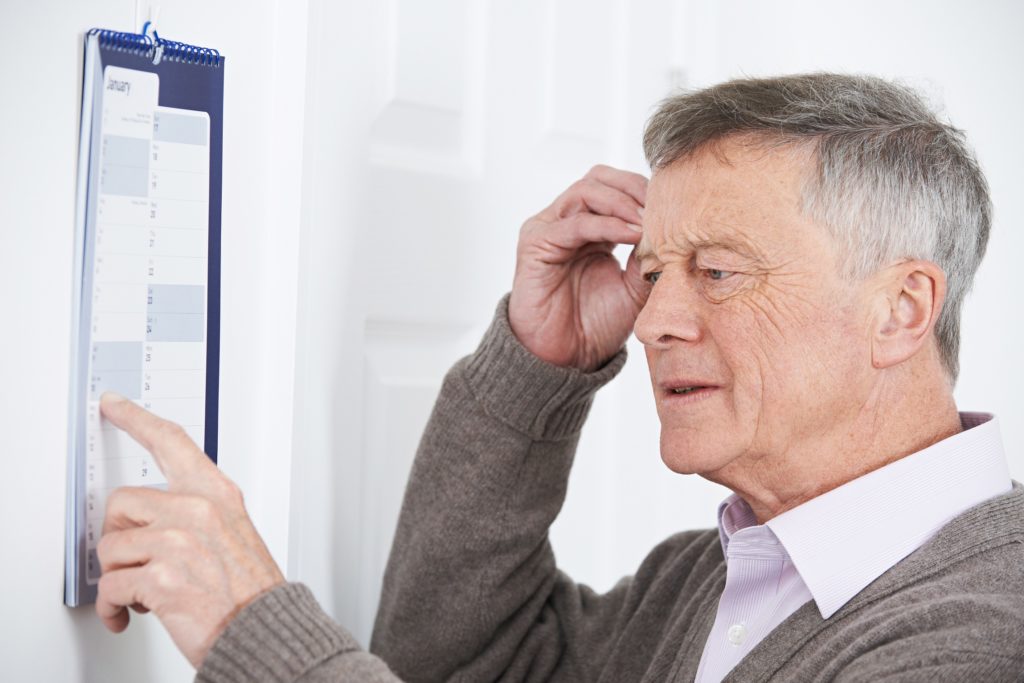 Confused Senior Man With Dementia Looking At Wall Calendar Confused Senior Man With Dementia Looking At Wall Calendar