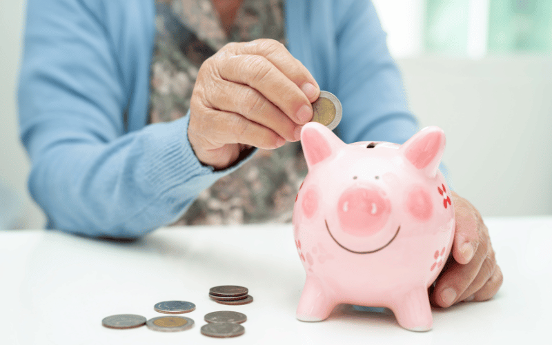 Elderly woman putting coin into pink piggy bank for saving