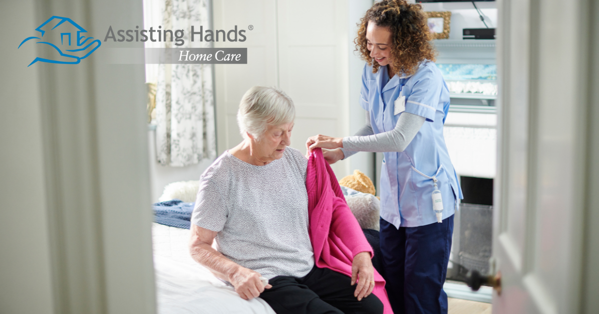 A professional caregiver helps a senior client get her coat on and get ready for the day.