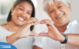 A daughter and an older mother create a heart with their hands, representing the feeling that is highlighted during National Family Caregivers Month