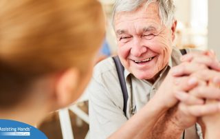 A caregiver holds hands with a happy older client, representing the results of creating a comfortable environment in the home.