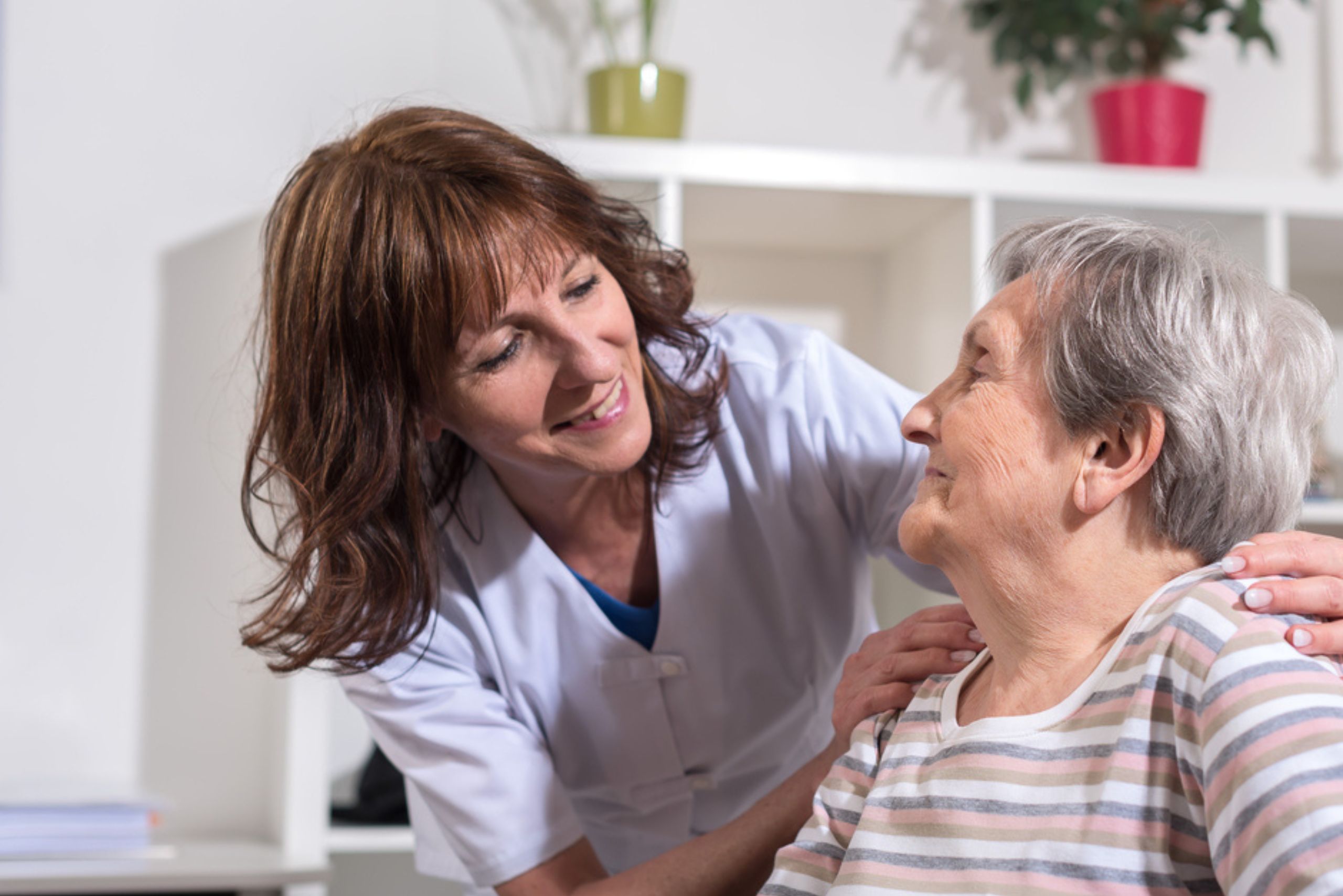 A caregiver comforting an elderly woman by resting hand on shoulder. Coordination of Care in Brookline