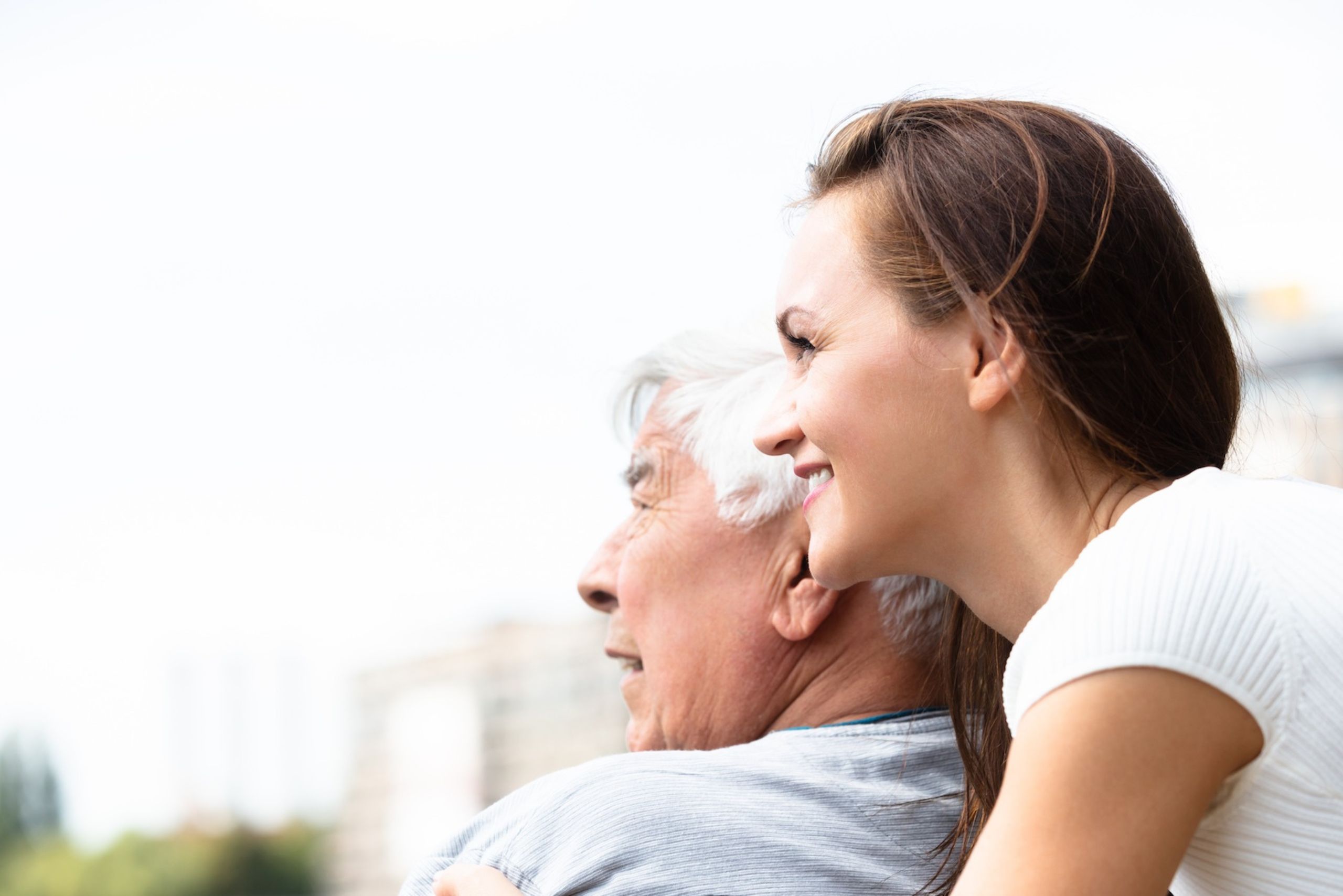 A cheerful care giver stands behind an elderly gentlemen looking off into the horizon. Veteran Care in Waltham