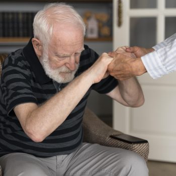 A elderly man holding hand of care giver as he is assisted with standing up from a chair. Parkinson's Care in Arlington