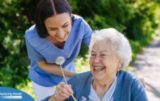 Caregiver and senior woman in wheelchair holding dandelion, picking wild flowers. Nurse and elderly woman enjoying a warm day in nursing home, public park.