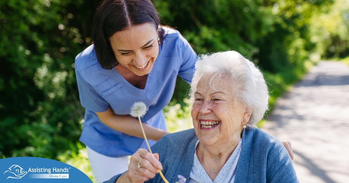 Caregiver and senior woman in wheelchair holding dandelion, picking wild flowers. Nurse and elderly woman enjoying a warm day in nursing home, public park.