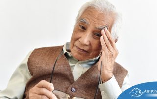 An older adult holds his head and his glasses representing vision problems like macular degeneration.