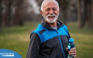 An older man smiles with a water bottle while exercising, representing the benefits of encouraging exercise when caring for seniors at home.