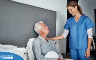 A caregiver smiles at an older client in bed, representing the compassion involved in being a live-in caregiver.