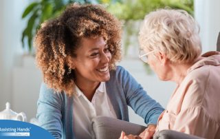 A caregiver smiles at an older client in a chair, representing the joy that can come from a healthy work-life balance.